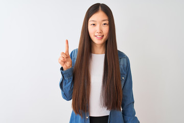 Young chinese woman wearing denim shirt standing over isolated white background showing and pointing up with finger number one while smiling confident and happy.