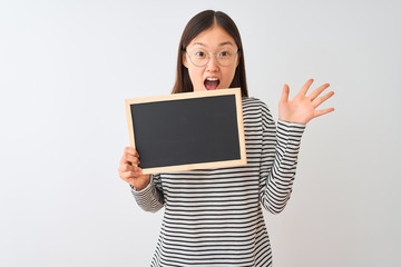 Naklejka premium Young chinese woman wearing glasses holding blackboard over isolated white background very happy and excited, winner expression celebrating victory screaming with big smile and raised hands