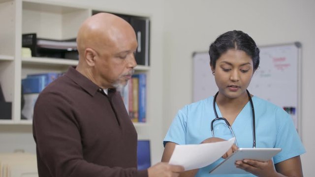 Nurse w/ stethoscope explains info on tablet and printout, slight camera move