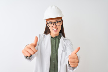 Young chinese engineer woman wearing coat helmet glasses over isolated white background approving doing positive gesture with hand, thumbs up smiling and happy for success. Winner gesture.