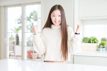 Beautiful Asian woman wearing casual sweater celebrating surprised and amazed for success with arms raised and open eyes. Winner concept.