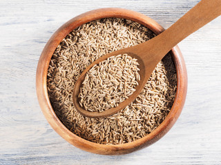 Cumin seeds (Cuminum), Jeera in a wooden scoop diagonally and cup on a white wooden background