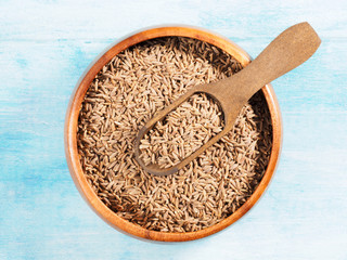 Cumin seeds (Cuminum), Jeera in a wooden scoop diagonally and cup on a blue old wooden background