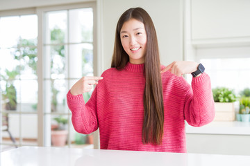 Beautiful Asian woman wearing pink sweater on white table looking confident with smile on face,...