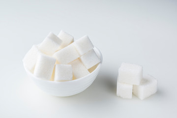 Sugar cubes in sugar bowl and near on white background