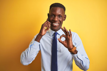 African american businessman talking on smartphone standing over isolated yellow background doing...