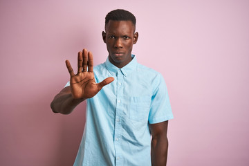 African american man wearing blue casual shirt standing over isolated pink background doing stop...