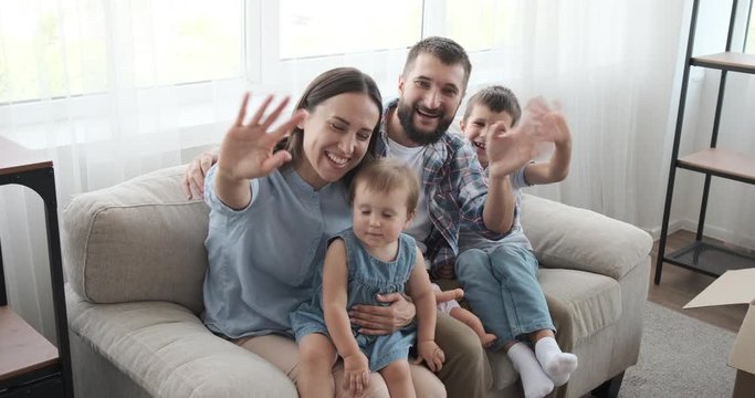 Portrait Of Happy Family Sitting On Sofa And Waving Hands In New House