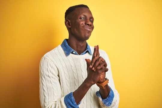 African american man wearing denim shirt and white sweater over isolated yellow background Holding symbolic gun with hand gesture, playing killing shooting weapons, angry face