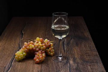 Glasses of white wine and a bunch of grapes on wooden table.