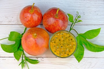Top view of ripen passion fruits and a glass of fresh passion fruits juice with green leaves on white wooden table.