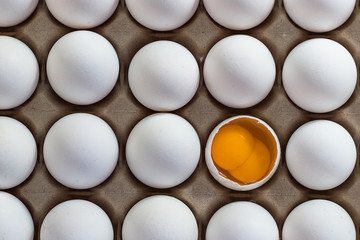 carton of white eggs with a broken two egg yolk