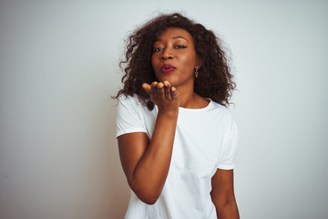 Fototapeta na wymiar Young african american woman wearing t-shirt standing over isolated white background looking at the camera blowing a kiss with hand on air being lovely and sexy. Love expression.