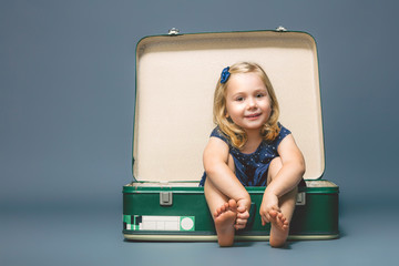 girl barefoot sitting inside an old suitcase.