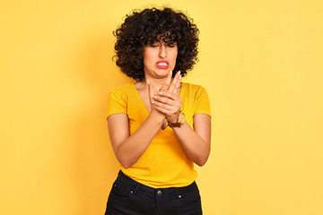 Young arab woman with curly hair wearing t-shirt standing over isolated yellow background Suffering pain on hands and fingers, arthritis inflammation