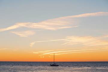 Fototapeta na wymiar Lonely boat floats on a quiet warm calm sea against the backdrop of a golden sunset on a warm summer evening. Advertising space