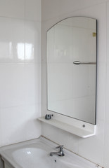 White ceramic sink with chrome tap and mirror on white tiles wall.