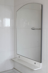 Mirror and plastic shelve on white tiles wall.