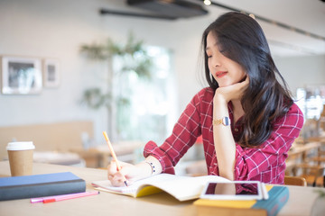 Young beautiful Asian woman reading a book while doing her homework in the modern co working space