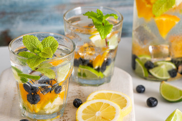 Summer healthy cocktails of citrus infused waters, lemonades or mojitos, with lime lemon orange blueberries and mint, diet detox beverages, in glasses on light background.