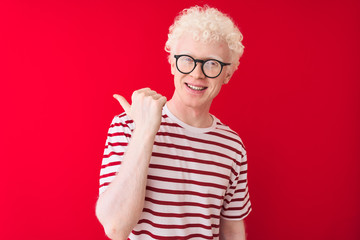 Young albino blond man wearing striped t-shirt and glasses over isolated red background smiling...