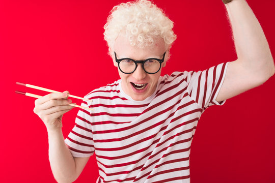 Young albino blond man holding chopsticks standing over isolated white background annoyed and frustrated shouting with anger, crazy and yelling with raised hand, anger concept