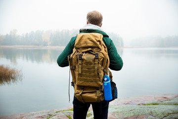 Mature man exploring Finland in the fall, looking into fog. Hiker with big backpack standing on...