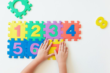 Child's hands playing with numbers, learning simple multiplication. Colorful bright puzzle numbers on white background, education concept