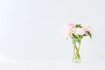 Pink and white peonies in a glass vase on a white background