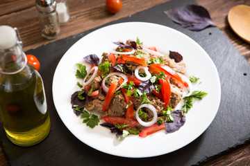 Fried liver with onion and tomatoes on black stone background