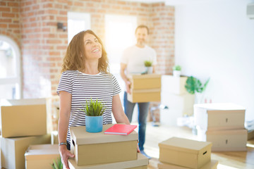 Middle age senior couple moving to a new house, smiling woman holding cardboard boxes and packaging