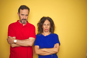 Beautiful middle age couple together standing over isolated yellow background skeptic and nervous, disapproving expression on face with crossed arms. Negative person.