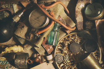 Different antique items on the table: bronze jewelry, old money, retro manometer, magnifier, glass bottle, silverware. Vintage background from a collection of antiques. Close-up selected focus