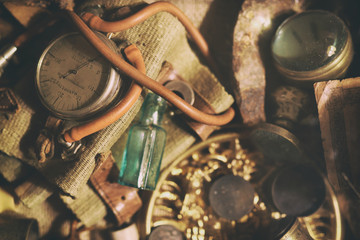 Different antique items on the table: bronze jewelry, old money, retro manometer, magnifier, glass bottle, silverware. Vintage background from a collection of antiques. Close-up selected focus