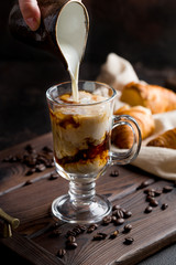 milk is poured into iced coffee on dark wooden tray with croissants