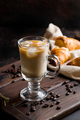 iced coffee with milk on dark wooden tray with croissants