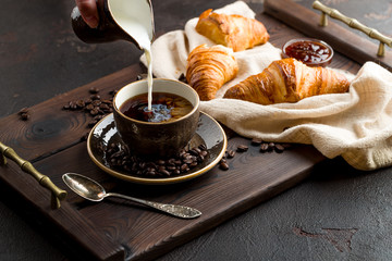 milk is poured into the coffee on a dark wooden tray with croissants