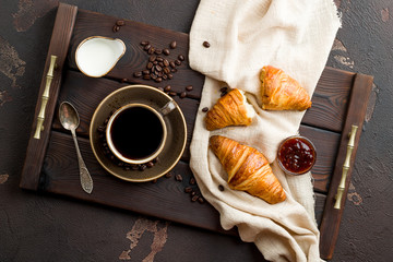 Cup of coffee with a croissant on a dark wooden tray