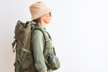 Middle age hiker woman wearing backpack canteen hat glasses over isolated white background looking to side, relax profile pose with natural face with confident smile.