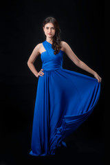 Cheerful young woman wearing blue dress standing and posing on isolates black background.Lady joyful and charming smile.