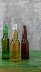 Three bottles of beer of different colors on a green table with gray industrial background