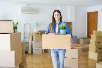Fototapeta na wymiar Beautiful young woman holding cardboard box at new apartment, smiling very happy moving to a new house