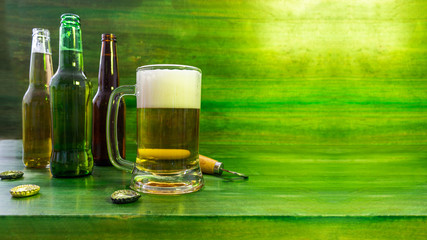 Group of multi-colored beer bottles with a jug served with foam on a green background