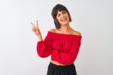 Young beautiful woman wearing red summer t-shirt standing over isolated white background smiling with happy face winking at the camera doing victory sign with fingers. Number two.