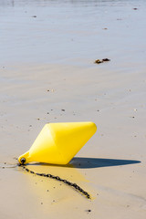 Close-up view of a large yellow buoy and its anchorage chain, used as a launching channel marker, lying on the wet sand on the beach in Penvenan, Brittany, France, under a bright sunshine.