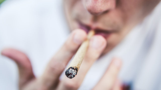 The Young Person Smoking Medical Marijuana Joint Outdoors. The Young Man Smoke Cannabis Blunt, Close-up.