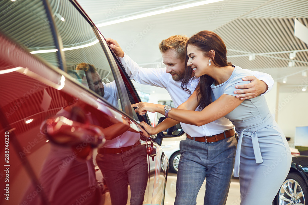 Wall mural Young couple choose a new car in showroom.