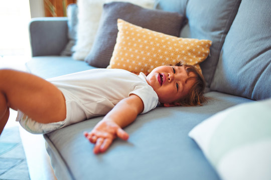 Beautiful toddler child girl wearing white bodysuit crying lying down on the sofa