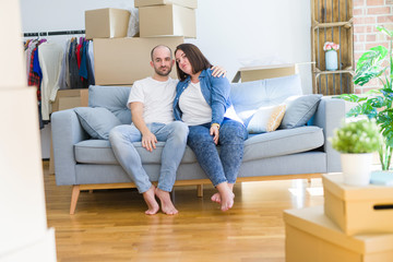 Fototapeta na wymiar Young couple sitting on the sofa arround cardboard boxes moving to a new house Relaxed with serious expression on face. Simple and natural looking at the camera.