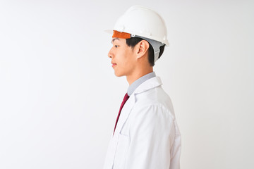 Chinese architect man wearing coat and helmet standing over isolated white background looking to side, relax profile pose with natural face with confident smile.